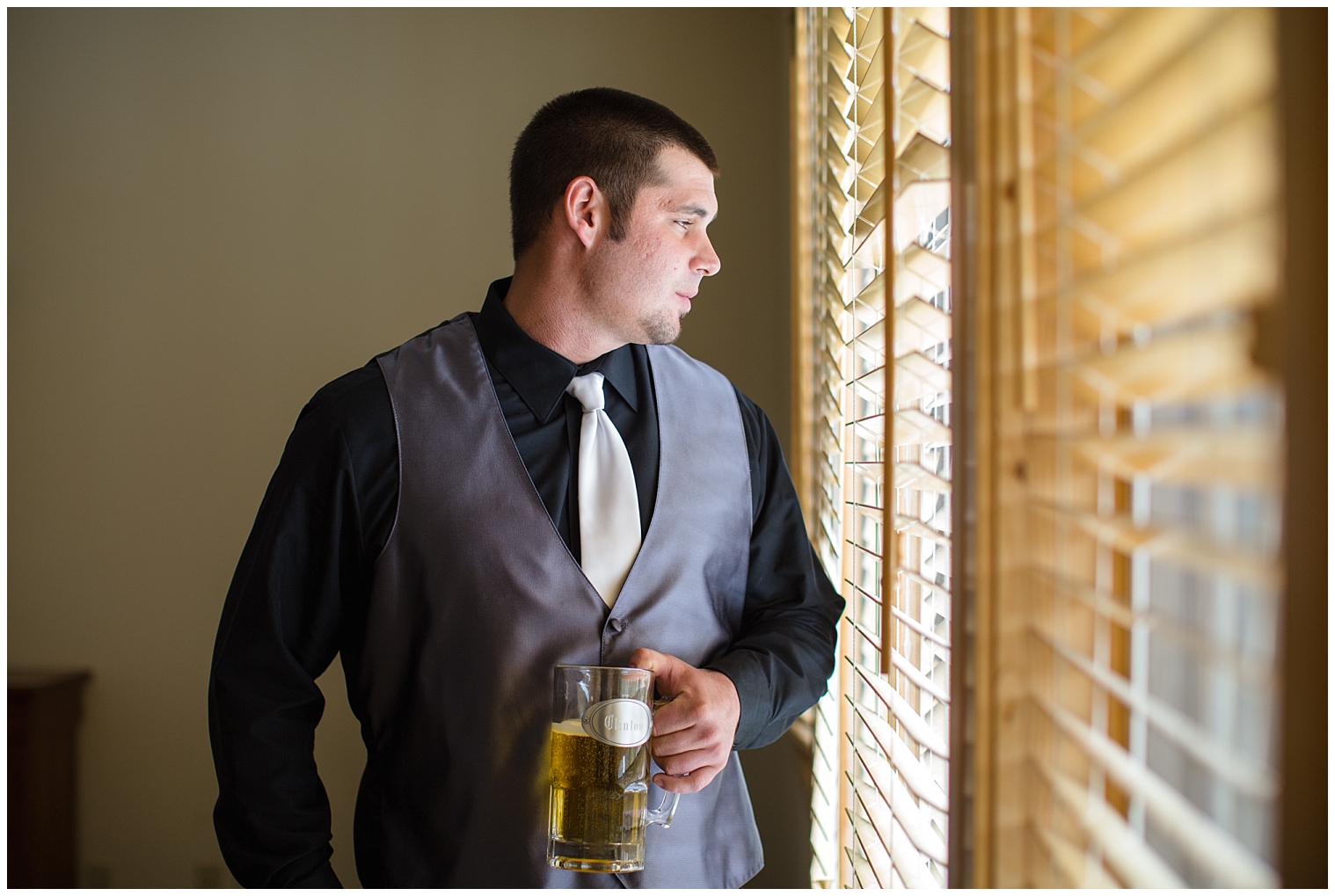 Groom holds a beer and looks out the window at his Breckenridge wedding.