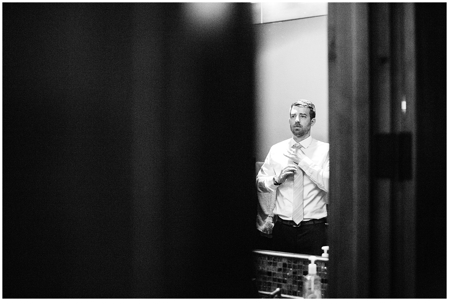 Groom looks in mirror while putting on his tie prior to his Copper mountain wedding.