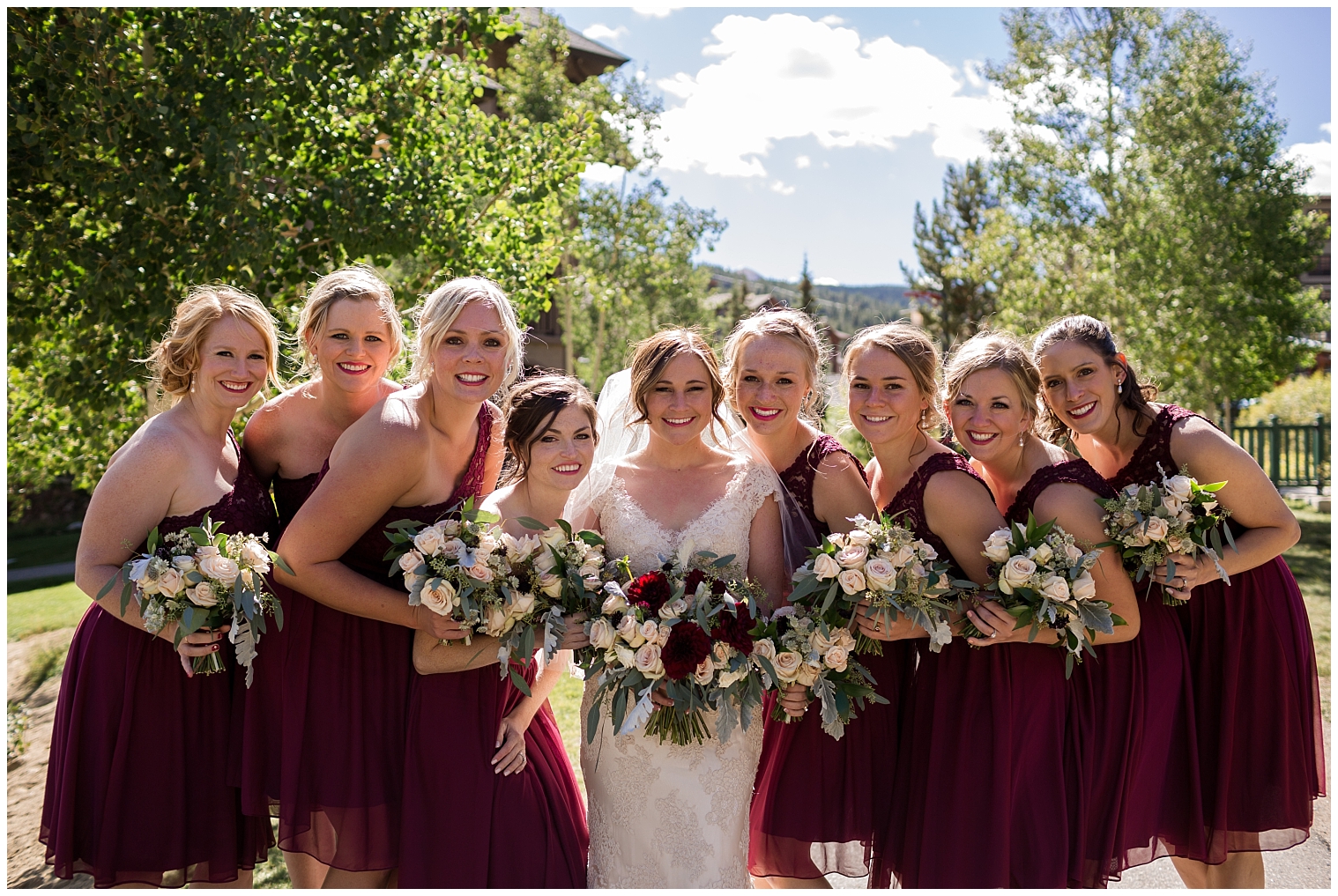 On her Copper Mountain wedding day, the bride poses with her bridesmaids wearing knee-length burgundy dresses.