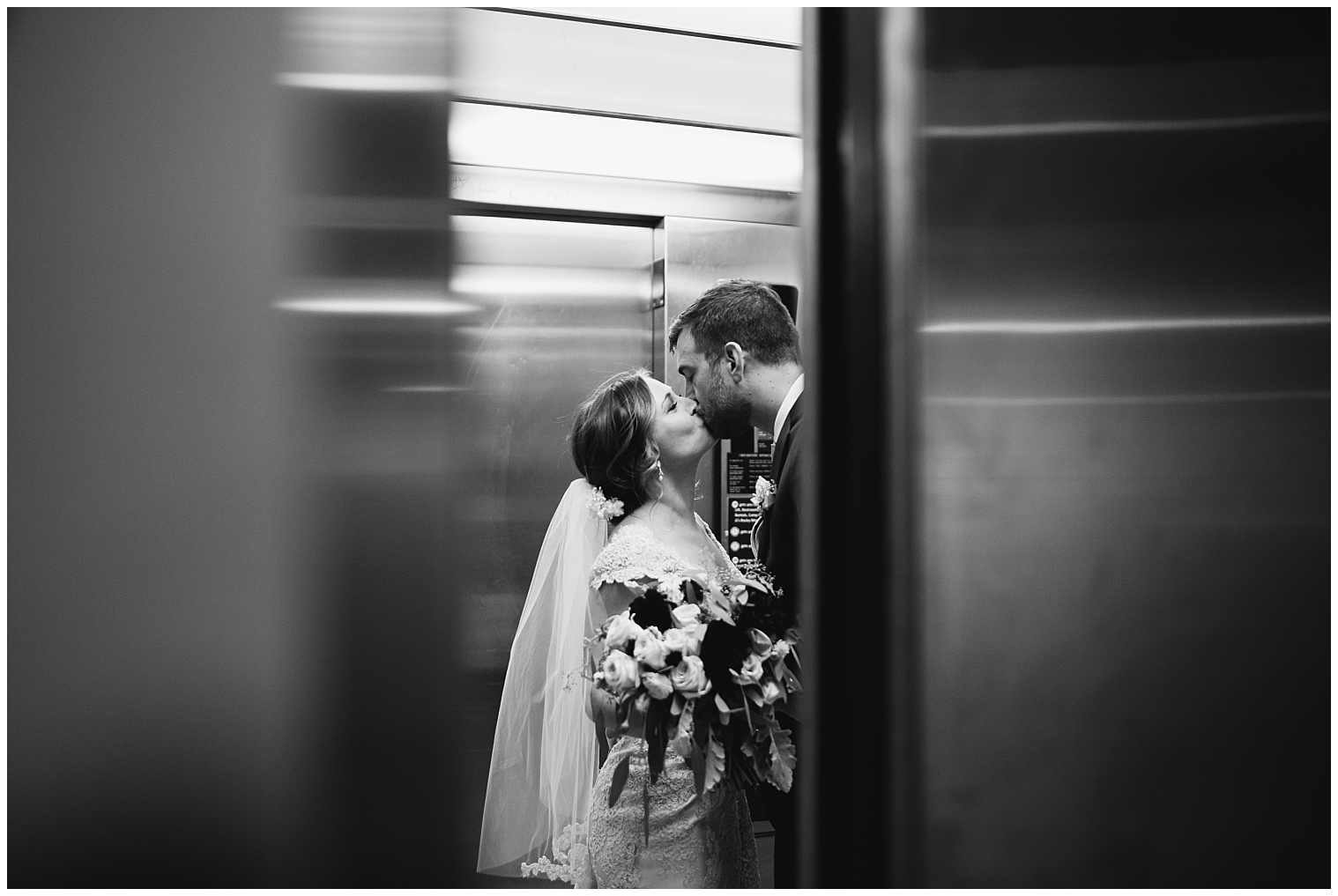A black and white photo captured by a Colorado wedding photographer of the bride and groom kisses in the elevator.
