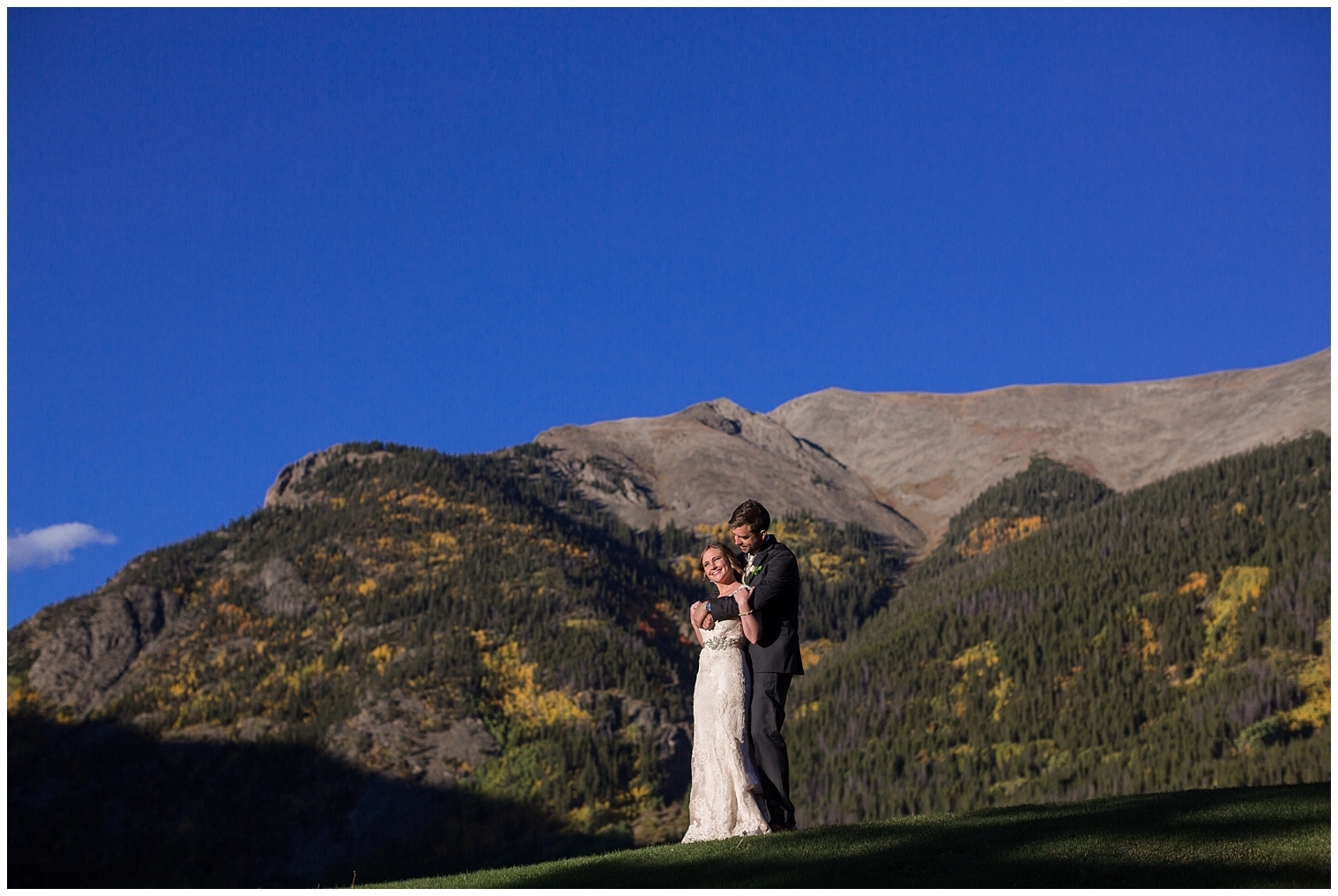 The wedding couple hug on a grassy knoll during portraits at their Copper Mountain wedding.