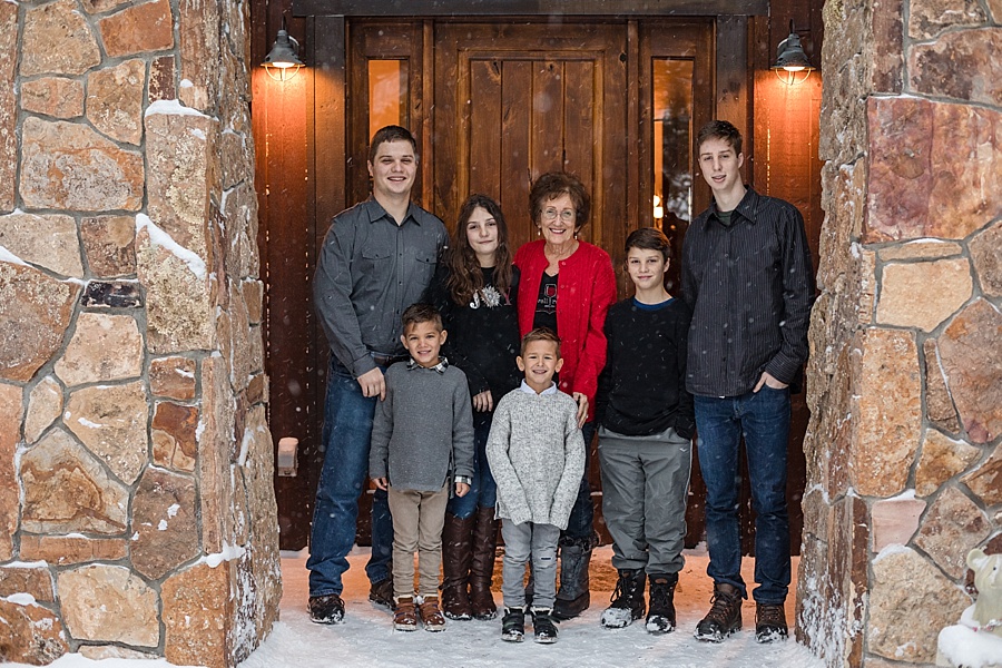 six grandchildren pose with their grandma in front of snowy cabin in Breckenridge Colorado 